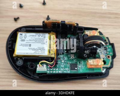 Disassembled wireless computer mouse showing internal circuit board, battery, and components on wooden surface Stock Photo