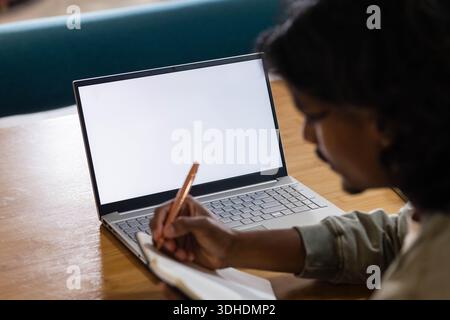 Open laptop is glowing with blank white screen on wooden table, notebook and pen resting Stock Photo