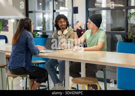 African American coworkers sitting and discussing at long table in coworking space with laptop Stock Photo