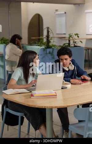 African American students studying in study lounge at wooden table with laptop, hoodie, headphones Stock Photo