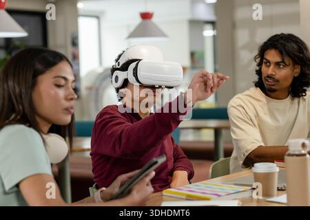 African American friends collaborating at study table, man reaching with white VR headset and phone Stock Photo