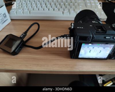 Digital camera connected to external device via USB cable on desk Stock Photo