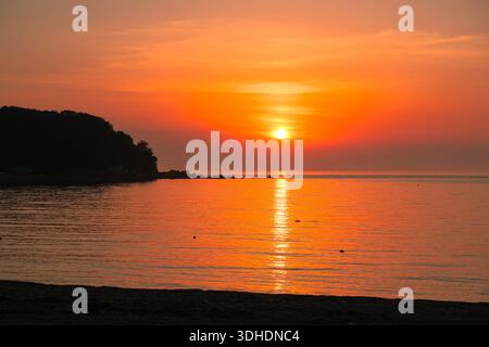 Golden sunset over a calm sea at Silmi Beach in Incheon, South Korea, with warm orange tones reflecting on the water during a peaceful summer evening. Stock Photo