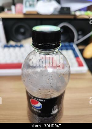 A close-up of a condensation-covered Pepsi bottle on a desk with keyboard and speakers in the background Stock Photo