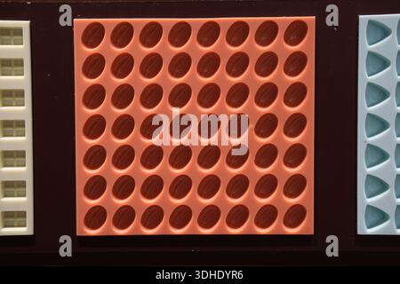 Top view of rectangular trays with repeated oval and triangular cavities in red, blue and cream tones, evenly spaced Stock Photo