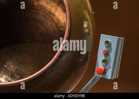 Angled view of industrial metal vessel and mounted control box with indicator lights and red button. Stock Photo