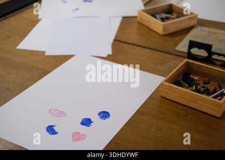 Sheets of paper with crayon drawings on wooden table surface. Stock Photo