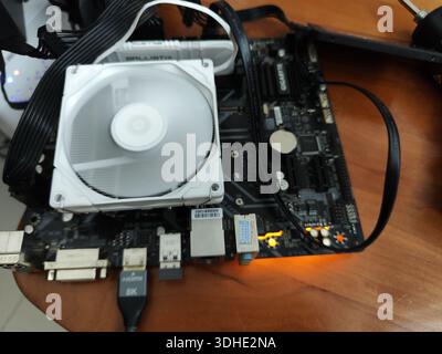 Close-up of Computer Motherboard with CPU Cooler and Cables on Wooden Surface Stock Photo