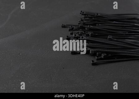 Neatly stacked black cable ties on a dark background with empty space. Minimal industrial background suitable for technology, repair, and organization Stock Photo