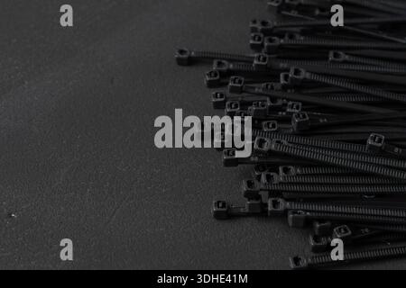 Pile of black cable ties arranged on a dark textured surface. Industrial still life illustrating organization, wiring, fastening, and technical work. Stock Photo