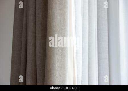 A close-up of layered beige and white curtains letting in gentle daylight. The textured fabric and soft lines evoke a calm, minimalist interior ideal Stock Photo