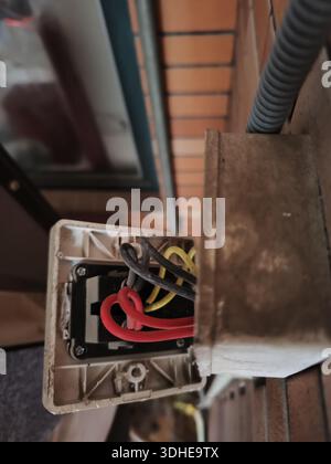 Open electrical junction box with wires exposed on a brick wall Stock Photo