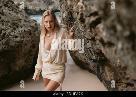Young blonde woman posing between coastal rocks on sandy beach Stock Photo