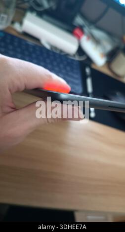 Hand holding a smartphone with glowing red indicator light on desk Stock Photo