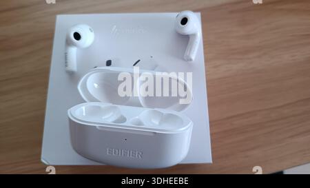 White Edifier wireless earbuds with charging case on wooden surface Stock Photo