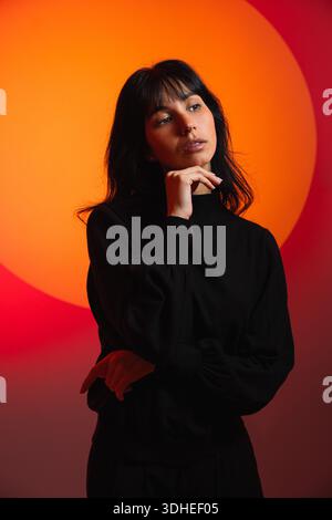 Woman contemplating future against vibrant orange circle background Stock Photo