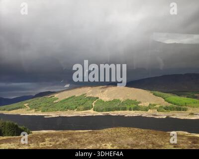 Stormy Sky Over a Mountain Reservoir with Rainfall and Green Hills Stock Photo