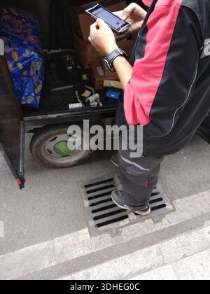 Person using smartphone while standing on a drainage grate next to a delivery cart Stock Photo