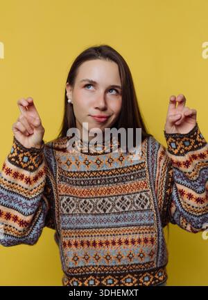Young woman in a patterned sweater making air quotes against a yellow background. Stock Photo