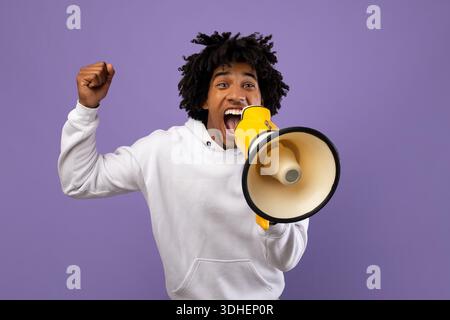 Agitated black teenager shouting into megaphone over violet studio background Stock Photo