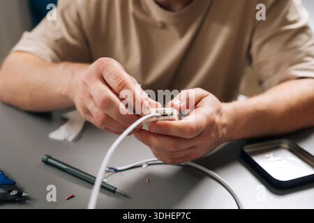 Close-up of male hands connecting white electrical cable to small housing unit, highlighting process of repairing and maintaining electronics, home Stock Photo