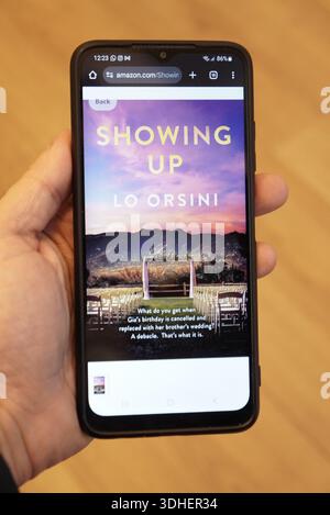 Smartphone displaying the book cover "Showing Up" by Lo Orsini on Amazon Stock Photo