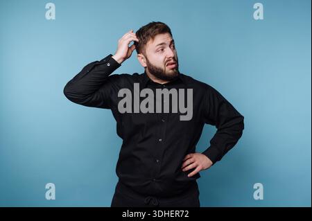 Man in black shirt scratching head with confused expression Stock Photo