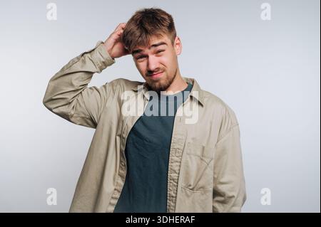 Young man scratching head, looking confused, wearing casual clothes. Stock Photo