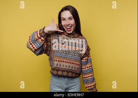 Smiling woman in a patterned sweater making a call me gesture. Stock Photo