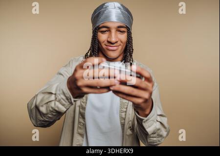 Young man with braids playing a game on his smartphone. Stock Photo