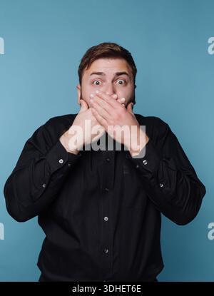 Man in black shirt covering mouth with surprised expression. Stock Photo