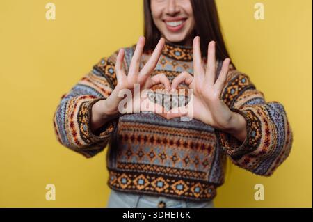 Woman in patterned sweater making heart shape with hands Stock Photo
