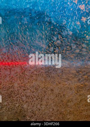 A macro close-up of intricate ice crystals and frost patterns on a window pane, illuminated by vibrant blue and warm orange backlighting during a cold Stock Photo