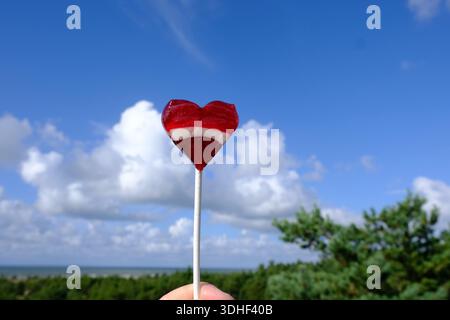 Latvian colours heart shaped lollipop against blue sky clouds background Stock Photo