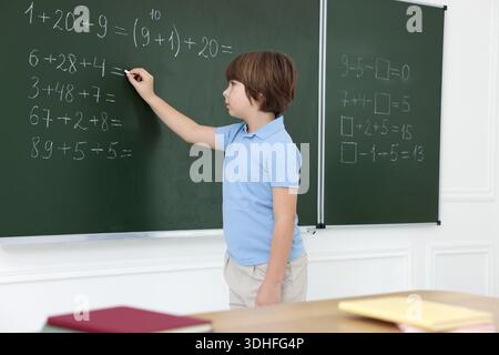 Schoolboy doing math on chalkboard in classroom Stock Photo