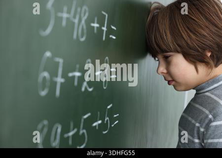 Schoolboy doing math on chalkboard in classroom Stock Photo
