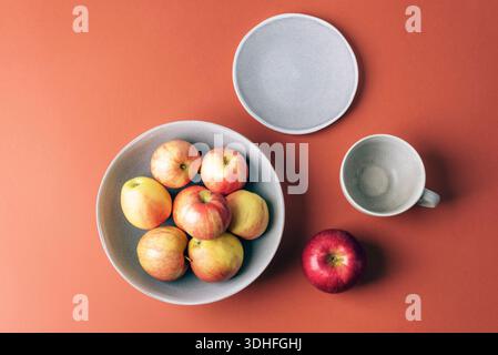 Fresh ripe apples in a bowl and empty cup with saucer on brown background. Top view, flat lay. Stock Photo