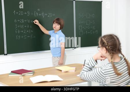 Schoolboy doing math on chalkboard in classroom Stock Photo