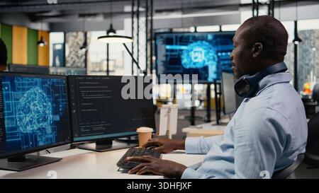 Data scientist in office doing software development to launch new features. African American man in startup company writing computer programs, doing code testing and quality assurance, camera A Stock Photo