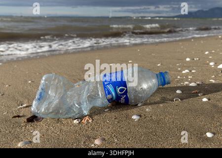 A discarded plastic water bottle lies on a sandy beach along the shoreline in Nadi, Fiji. Stock Photo