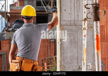 A worker uses a paint roller to apply paint on a wall at a construction site in daylight hours. Stock Photo
