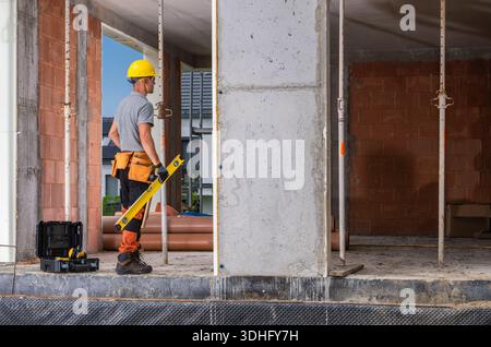 A construction worker stands at a site using a level tool on a wall. Stock Photo