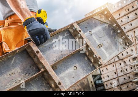 A construction worker holds a metal form for concrete while working on a construction site during the day. Stock Photo