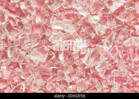 A close-up macro view of clear, broken glass pieces scattered across a soft pink background, creating a sparkling abstract texture Stock Photo