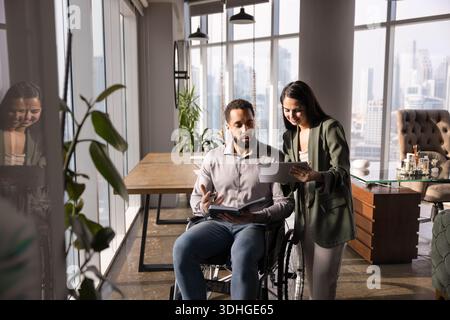Positive young female manager asking coworker with disability for advice Stock Photo