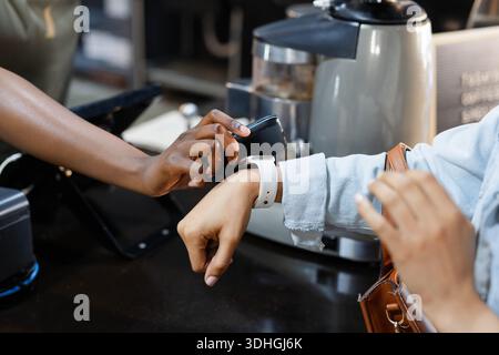 Left wrist wearing white smartwatch tapping black card reader on cafe countertop, POS and tan strap Stock Photo