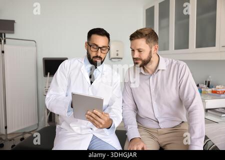 Confident doctor holding digital tablet explaining male patient medical data Stock Photo
