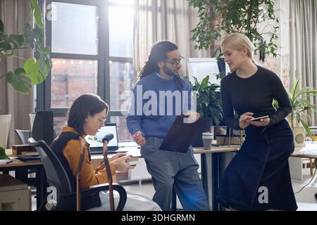 Multiethnic Coworkers Collaborating with Colleague with Disability in Office Stock Photo