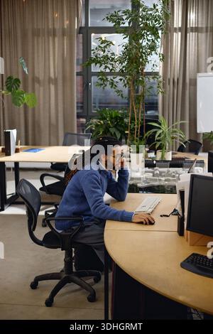 Young Adult Black Man Concentrating While Using Desktop Computer in Office Stock Photo