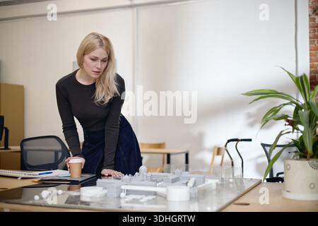 Young Adult Caucasian Woman Analyzing Architectural Model While Standing Indoors Stock Photo